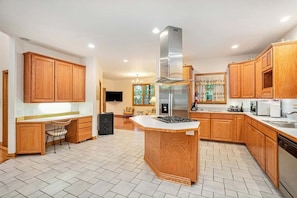 A modern kitchen with wooden cabinets, a central island, stainless steel appliances, and a tiled floor. - Great Escape: Spacious, Home Theater, Fire Pit, Walk to Downtown (Saugatuck)