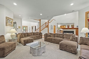 A spacious living room with a large sectional sofa, a glass coffee table, and a staircase leading to another level.