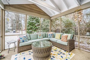 Une terrasse couverte avec un canapé d’angle, une table ronde en osier et un tapis à motifs.