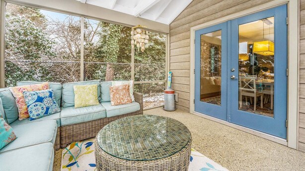 Un portico coperto con un divano azzurro, un tavolino in vimini e una porta vetrata che dà su un ambiente interno.