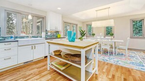 Una cucina moderna con mobili bianchi, un'isola in legno e un'area pranzo con sedie e tavolo bianchi.