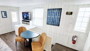 A room with a dining table, wicker chairs, a television, a fire extinguisher, and a sign on the wall. - Anchors Away: Nautical downtown Saugatuck abode with balcony and partial river views (Saugatuck)