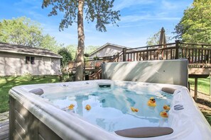 A hot tub with rubber ducks, surrounded by a wooden deck and a house.