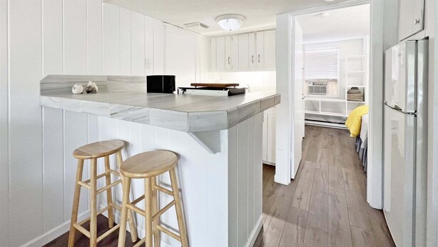 A kitchen with white cabinetry, a grey countertop, two wooden stools, and a stainless steel refrigerator.