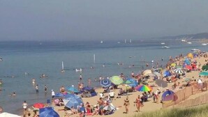 A crowded beach with people swimming and sunbathing, and a variety of colorful umbrellas.