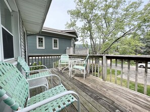 Une véranda abritée avec des meubles d’extérieur, une terrasse en bois et une vue sur une rue et des arbres.