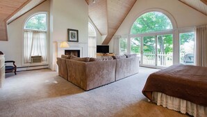A spacious loft bedroom with a large bed, a sofa, a fireplace, and a television.