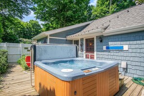Een hottub in een achtertuin met een houten terras, een wit hek en een huis met een grijze pannendak.