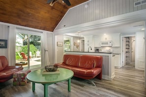 Uma sala de estar ampla com um sofá de couro vermelho, uma mesa de centro verde e uma cozinha ao fundo.