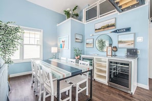 A dining area with a long table, chairs, a refrigerator, and a wall-mounted sign reading 'LAKE'.