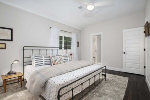 A bedroom with a bed, a nightstand, a window with curtains, a door, and a ceiling fan.