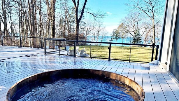 A hot tub on a wooden deck with a view of a grassy area and trees. - Pine Lodge: Lake Michigan Beach Access, Private Swimming Pool & Hot Tub, Sauna (Glenn)