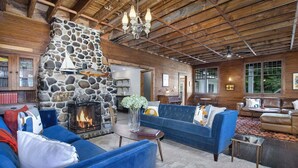 A rustic interior with a stone fireplace, wooden ceiling, and blue sofas. - Pine Lodge: Lake Michigan Beach Access, Private Swimming Pool & Hot Tub, Sauna (Glenn)