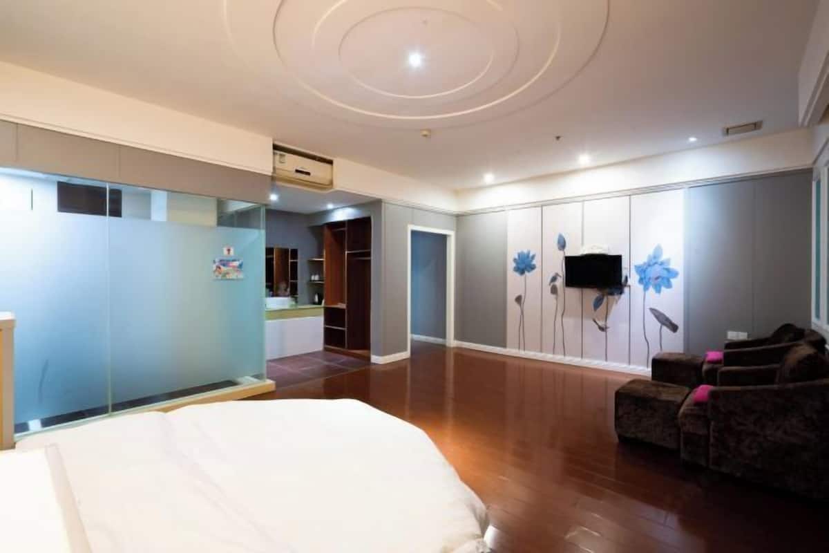 A bedroom with a bed, a seating area with a sofa, a wardrobe, and a television mounted on the wall.