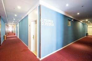 Pasillo de hotel con alfombra roja, paredes azules y una puerta con un cartel.