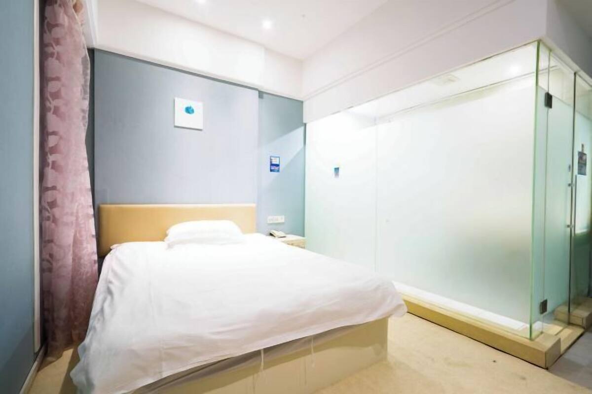 A hotel room with a bed, a nightstand, a glass-enclosed wardrobe, and a blue accent wall.