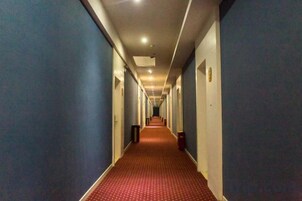 Un pasillo de hotel con alfombra roja, paredes azules y puertas a ambos lados.