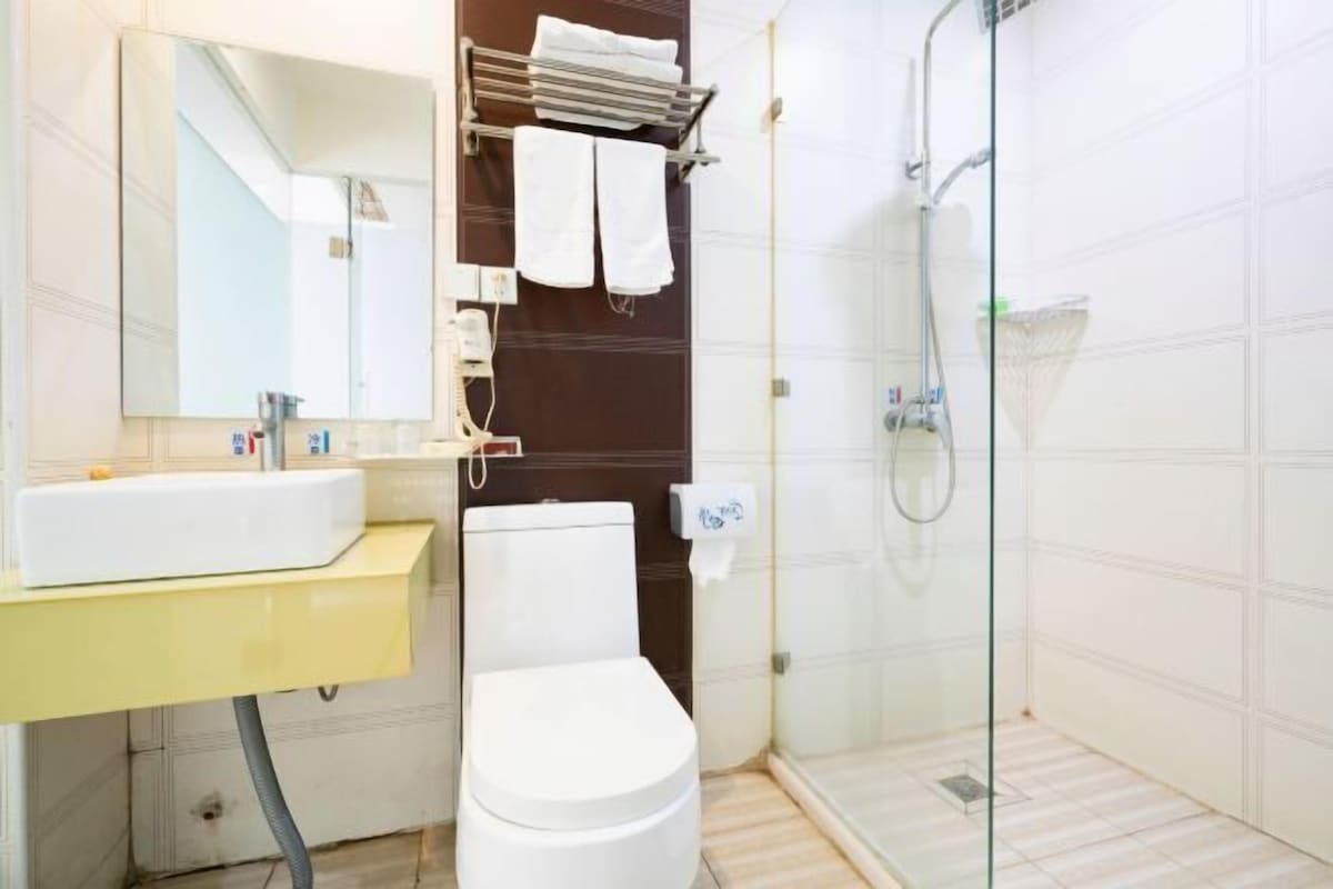Un baño con lavamanos blanco, espejo, inodoro y cabina de ducha con mampara de vidrio.