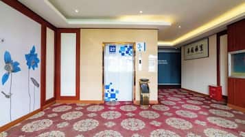 A hotel lobby with a patterned carpet, a reception desk, and a wall with a floral mural.