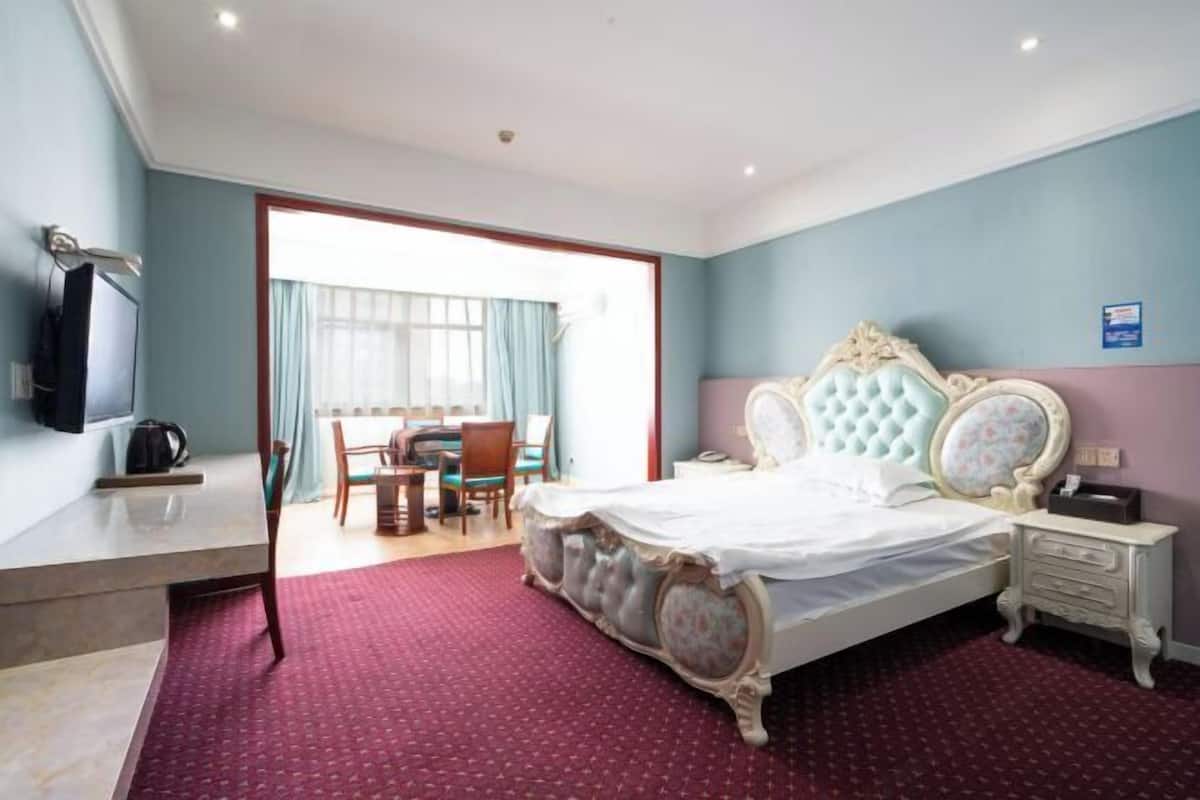 A hotel room with a large bed, a desk with a chair, a television, and a window with curtains.