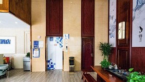 A hotel lobby with a wooden reception desk, a bench, a small table with items, and a wall with artwork. - Linhai H Chain Lihao Star Hotel (Linhai)