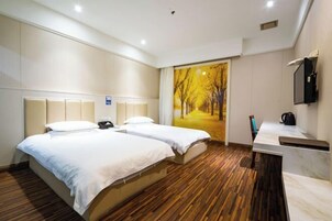 Habitación de hotel con dos camas, piso de madera, un ventanal con vista a un bosque, un escritorio con espejo y un televisor montado en la pared.