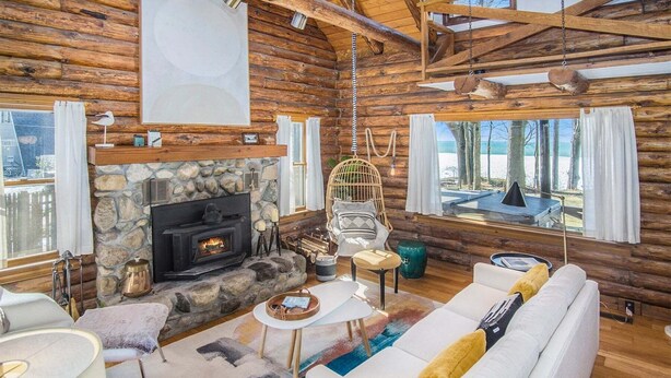 A log cabin interior with a stone fireplace, white sofa, and a hanging chair. - Lagom Sunset Retreat: Hot Tub, Lake Michigan Beach, Home Theater, Sunset Views (Fennville)