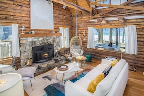 A log cabin interior with a stone fireplace, white sofa, and a hanging chair.