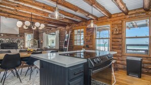 A log cabin kitchen with a central island, wooden beams, and large windows. - Lagom Sunset Retreat: Hot Tub, Lake Michigan Beach, Home Theater, Sunset Views (Fennville)