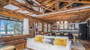 A log cabin interior with a white sofa, dining table, and kitchen area. - Lagom Sunset Retreat: Hot Tub, Lake Michigan Beach, Home Theater, Sunset Views (Fennville)