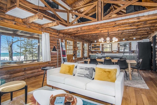 A log cabin interior with a white sofa, dining table, and kitchen area.
