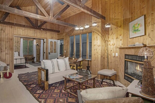 A wooden interior with a sofa, a coffee table, a fireplace, and a bed. - Bluffside: Lake Michigan Beach Access, Screen Porches, Fire Pit, Sunset Views (Glenn)