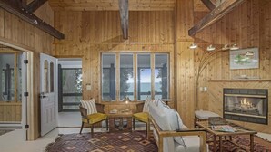 Interior acolhedor de uma cabana com lareira, paredes de madeira, uma janela grande e um tapete estampado.