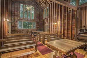 Un intérieur rustique en bois, avec des bancs et une table, de grandes fenêtres et un panneau indiquant la sortie.