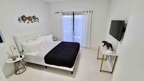 A bedroom with a bed, a bedside table with a lamp, a TV on the wall, and a small statue on a side table. - 302 Rare find The Blue Sky Beach House (Florida City)