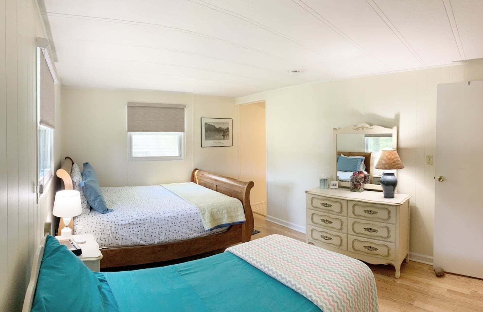 A bedroom with a bed, bedside table, lamp, dresser, mirror, and a window.