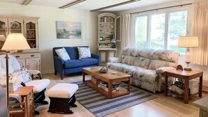 A living room with a blue sofa, a patterned sofa, a coffee table, and a bookshelf. - Bevlyn Cottage: Walk to Lake Michigan, Charming Cottage w/ Deck & Fire Pit (Douglas)
