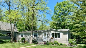 A single-story house with a front porch, a small garden, and a clear blue sky. - Bevlyn Cottage: Walk to Lake Michigan, Charming Cottage w/ Deck & Fire Pit (Douglas)