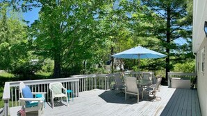 A wooden deck with outdoor furniture, including chairs and a table, and a blue umbrella. - Bevlyn Cottage: Walk to Lake Michigan, Charming Cottage w/ Deck & Fire Pit (Douglas)