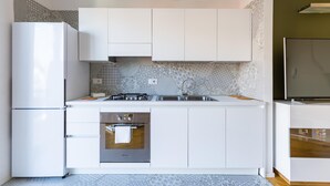A modern kitchen with white cabinets, a built-in oven, a stainless steel sink, and a refrigerator. - Chiaia Mon Amour Elegant Flat by Napoliapartments (Naples)