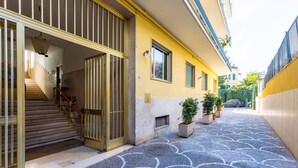 A building with a yellow facade, a staircase leading to a door, and a tiled pathway. - Chiaia Mon Amour Elegant Flat by Napoliapartments (Naples)