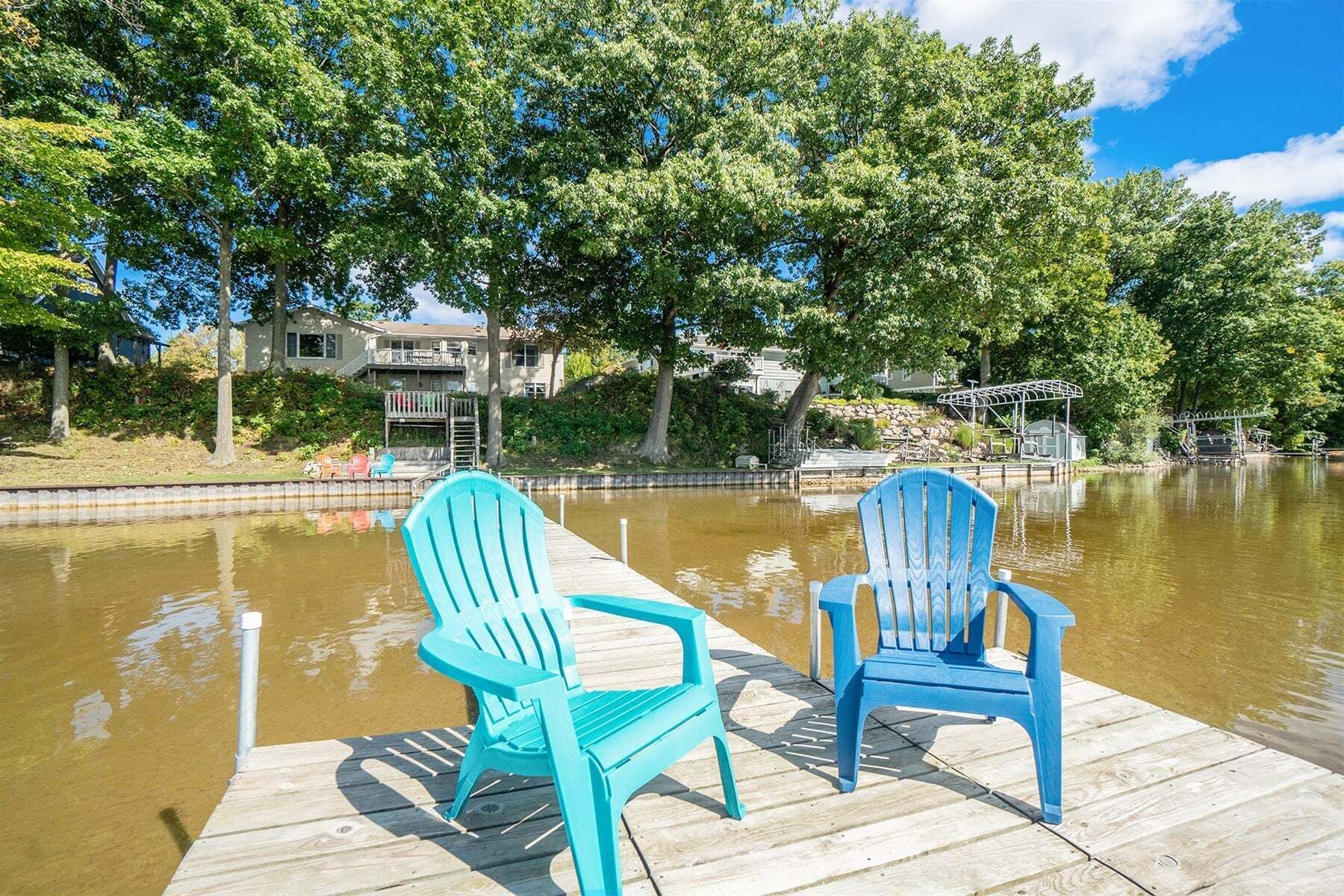 A wooden dock with two chairs facing a body of water, surrounded by trees and a residential area.