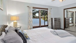 Un dormitorio con una cama grande, ventilador de techo, ventana con cortinas, lámpara y cómoda.