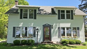 A two-story house with a front porch, a chimney, and a well-maintained lawn. - Summer Haven: Lake Michigan Views, Fire Pit, BBQ, Classic Cottage (Fennville)
