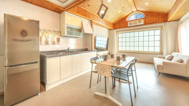 A modern kitchen with a built-in refrigerator, a dining area with a table and chairs, and a large window providing natural light. - Sokcho Seohyeon Ine Pension (Sokcho)