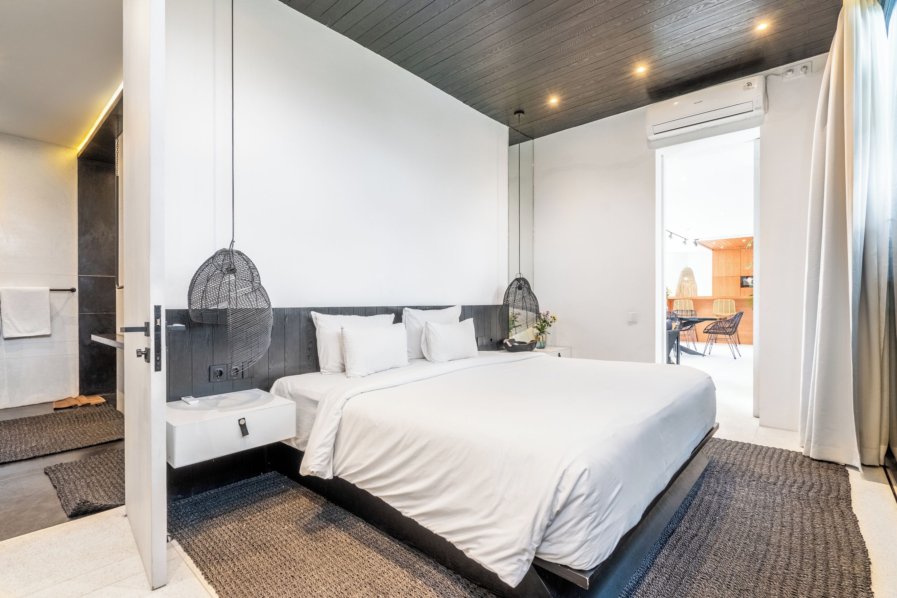 A modern bedroom with a large bed, bedside tables, a hanging light fixture, and a view of the outdoor area.