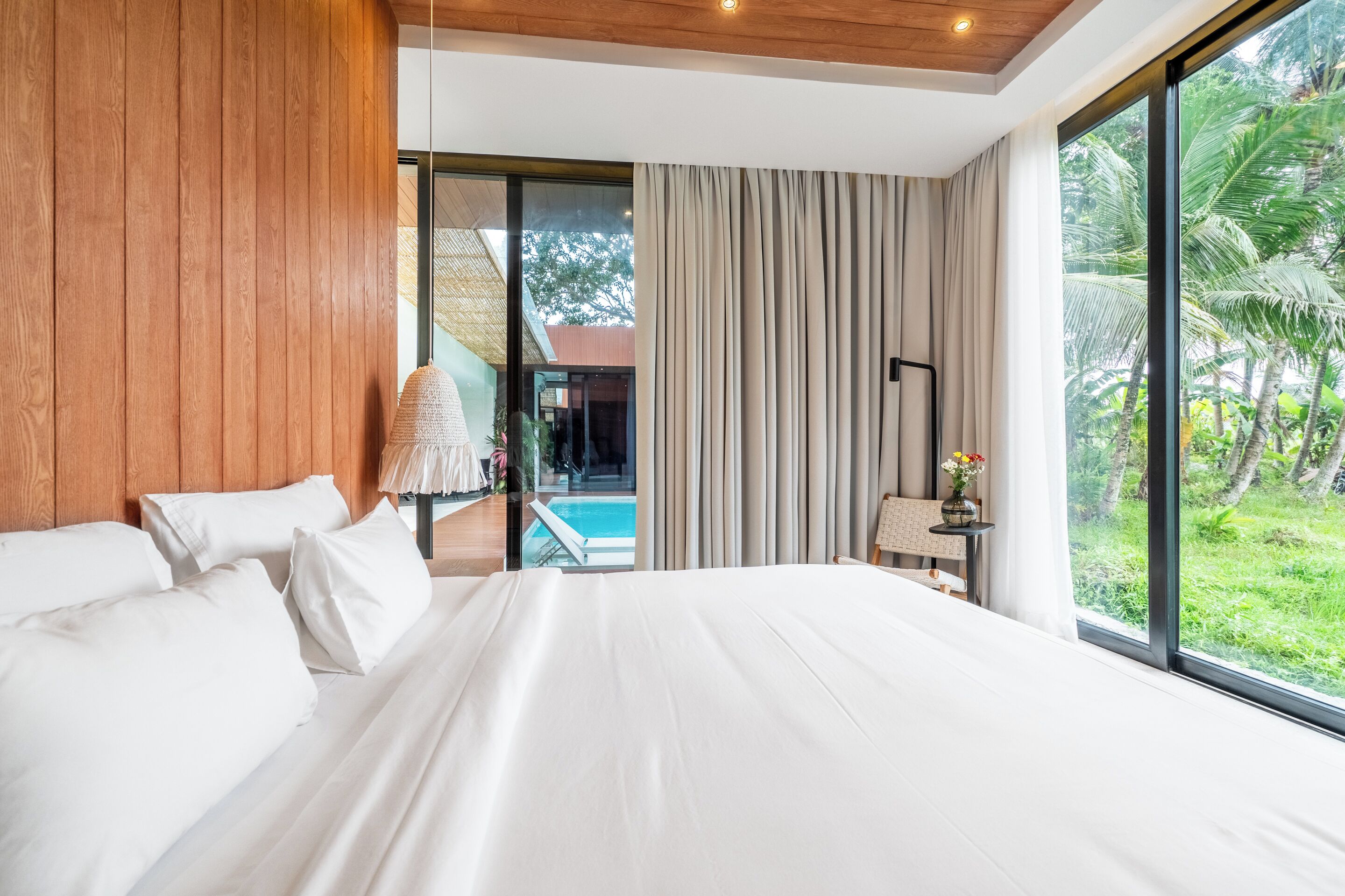 A modern hotel room with a large bed, a view of a swimming pool, and a balcony with a view of greenery.
