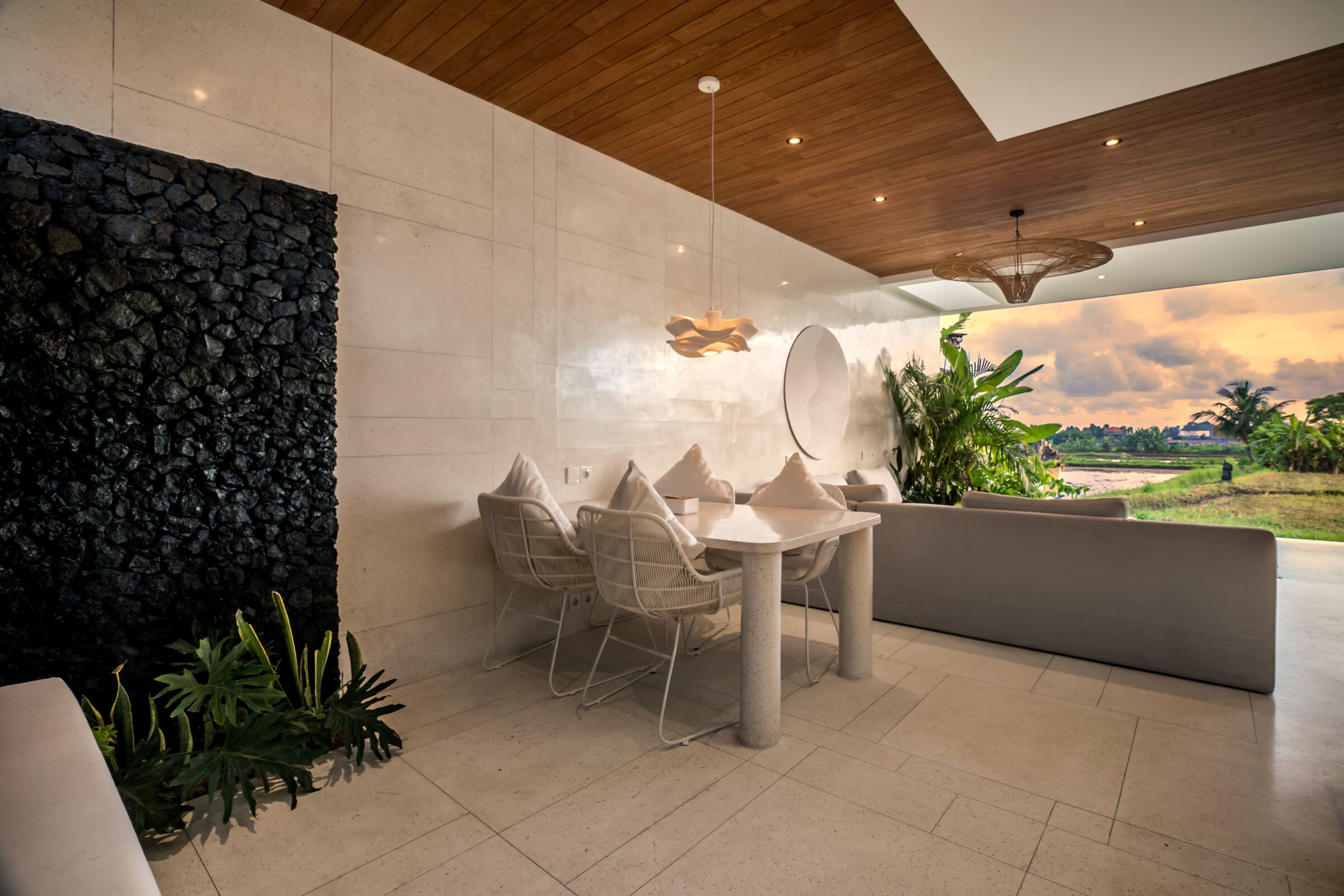 A modern dining area with a stone wall, a round table with chairs, and a view of the landscape.