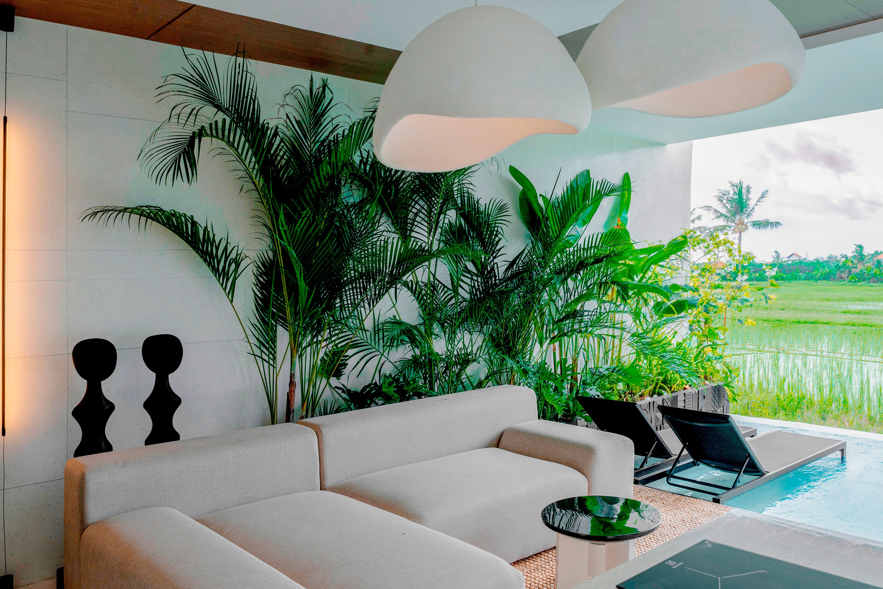 A modern living room with a white sofa, a coffee table, and a view of a swimming pool.