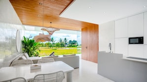 Cozinha moderna com armários brancos, teto de madeira e vista para uma paisagem verde.